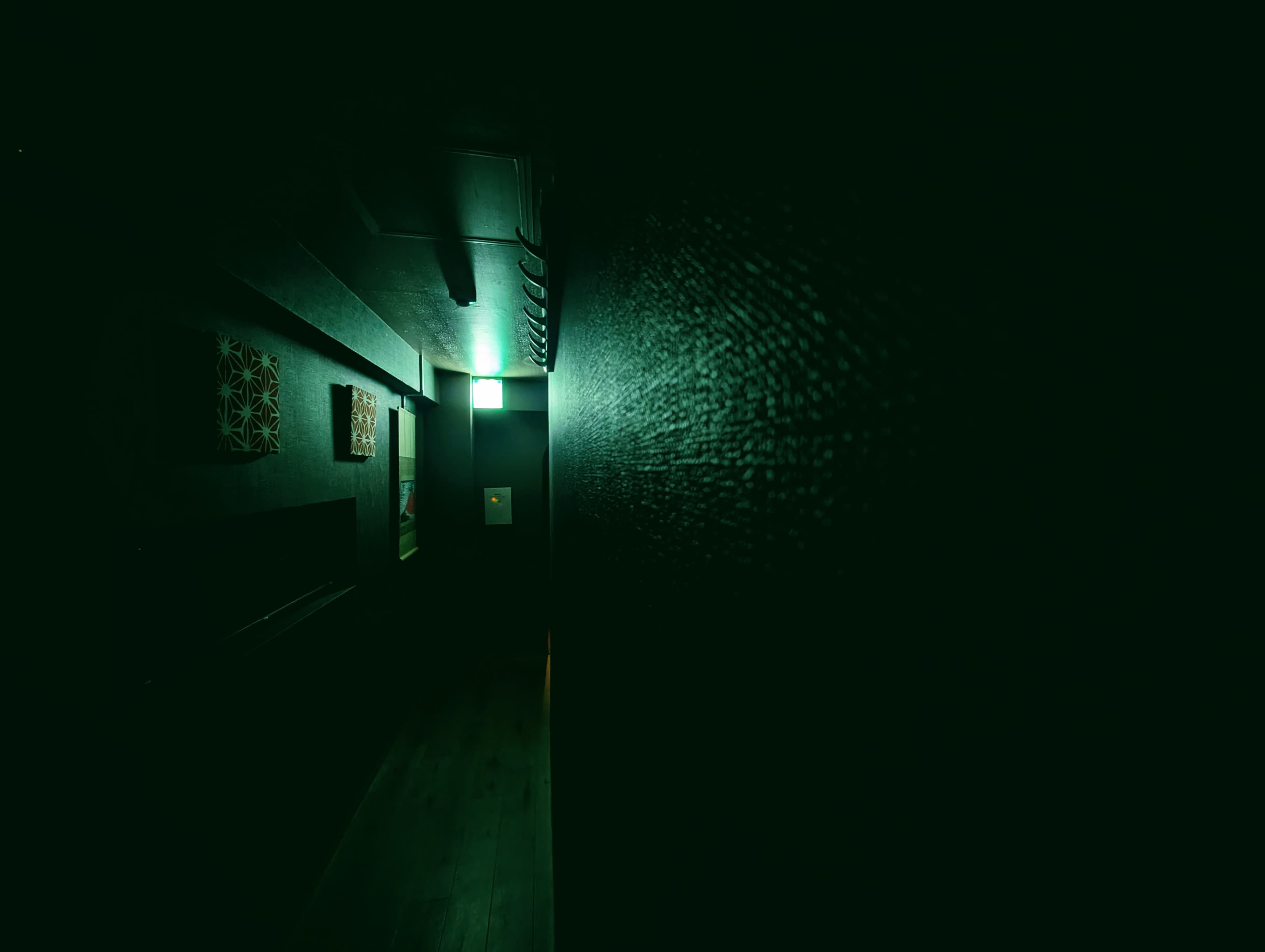 A green light at the end of a dark hallway in Tokyo.
