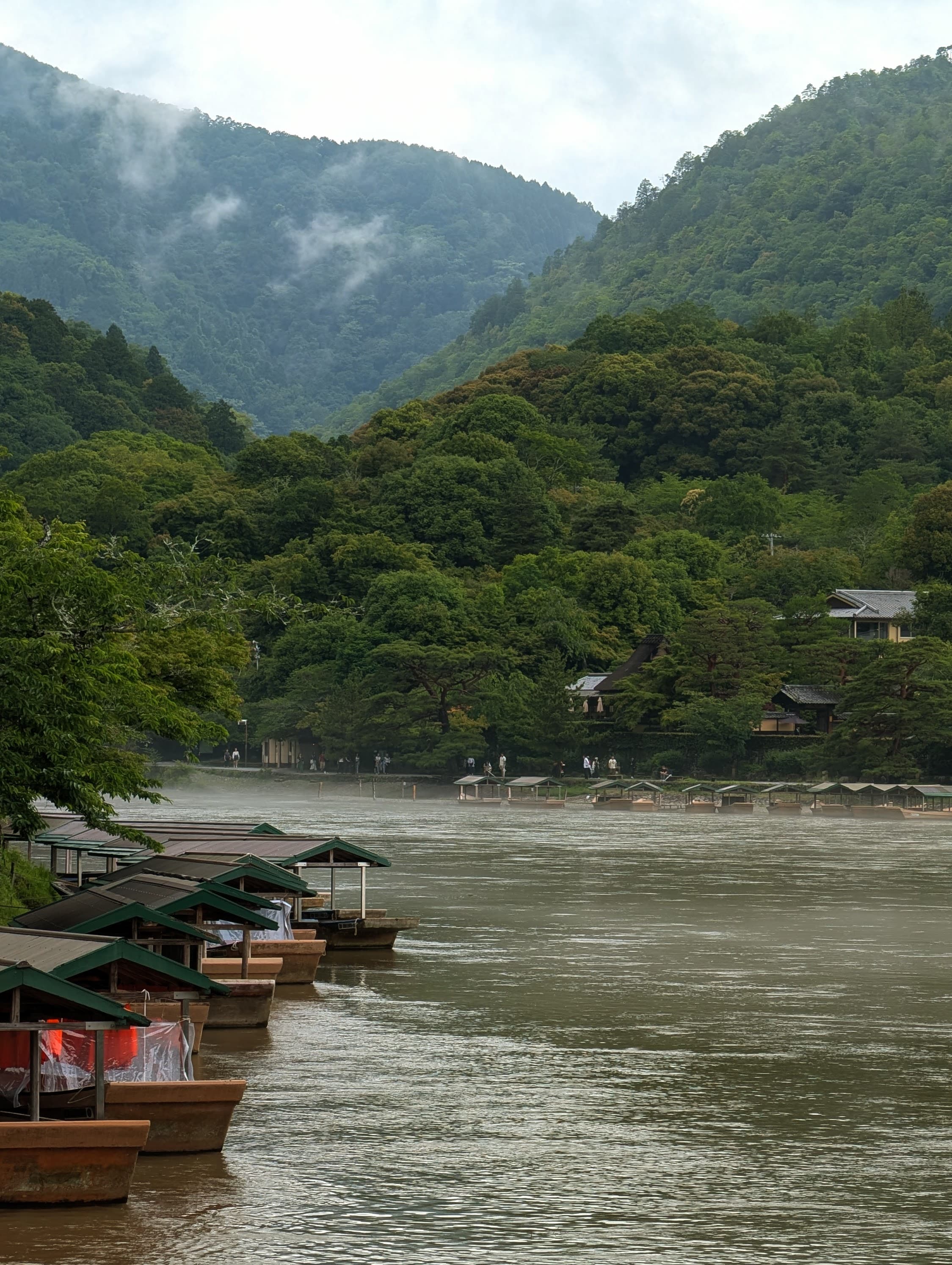Boats along the river below misty hills in Kyoto.