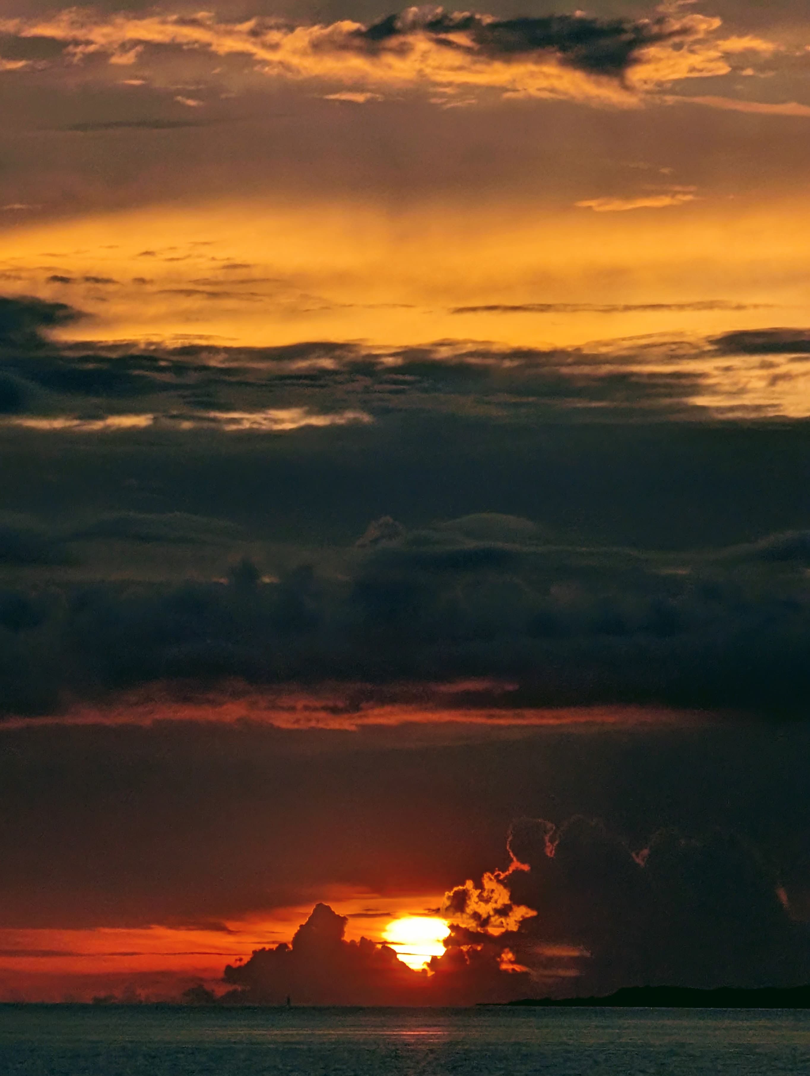 The sun dropping below dark clouds over the water in Motobu, Okinawa.