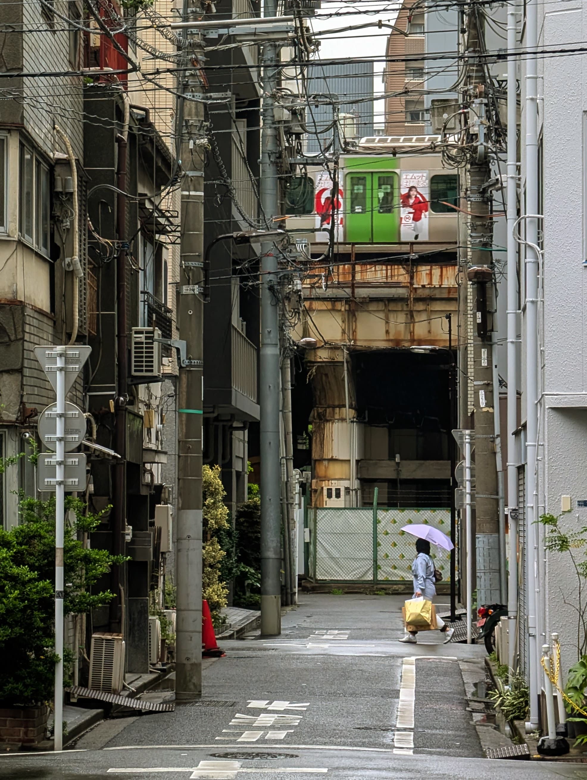 An umbrella on a narrow Tokyo street, with a train passing overhead.
