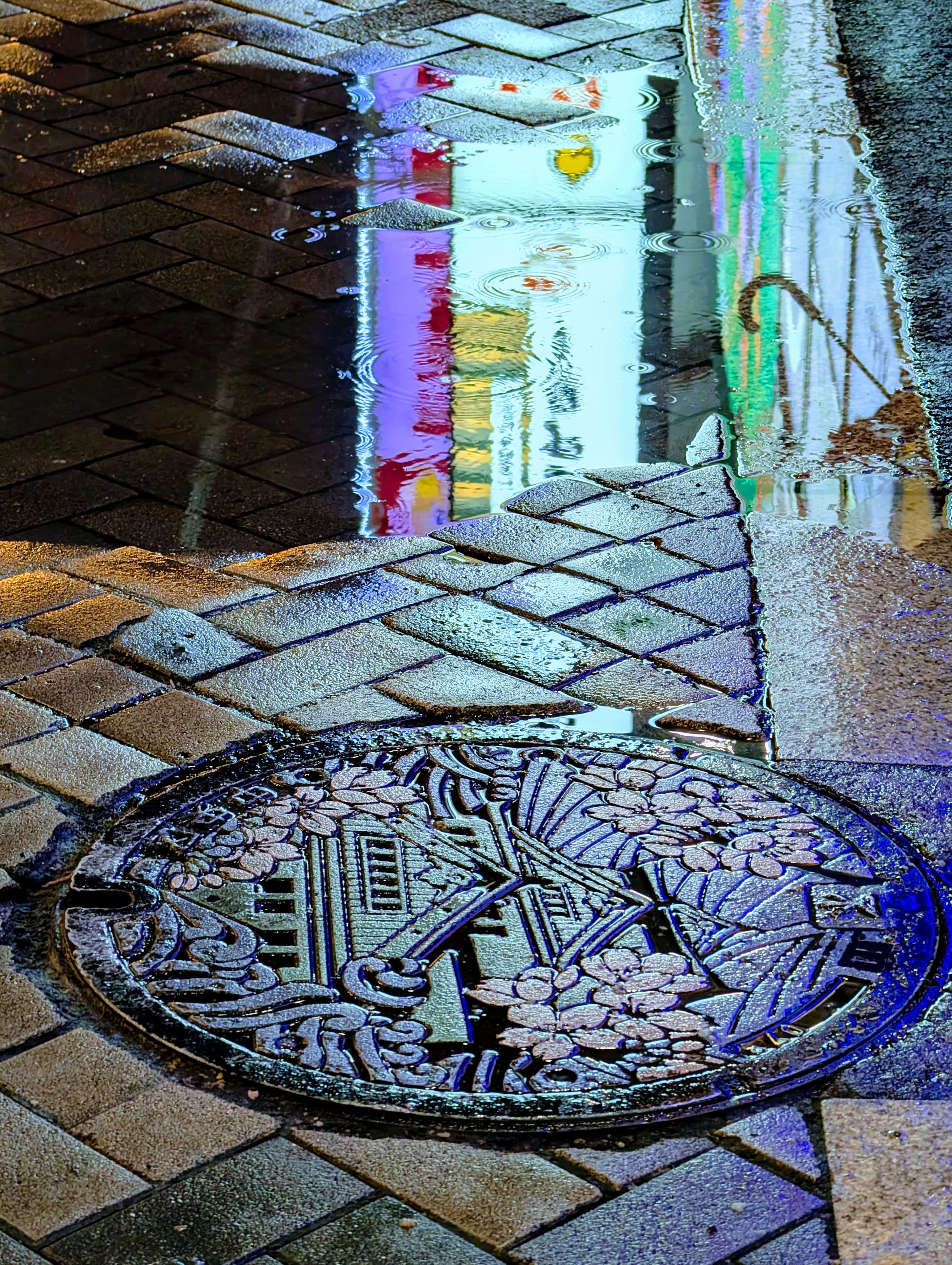 Colorful signs reflected beside a manhole cover in Osaka.
